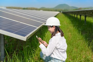 A female engineer wearing helmet in Photovoltaic Cell Farm or Solar Panels Field, eco friendly and clean energy.
