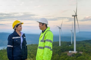 portrait of people engineer are standing in a field wearing a protective helmet on her head over electrical turbines background .