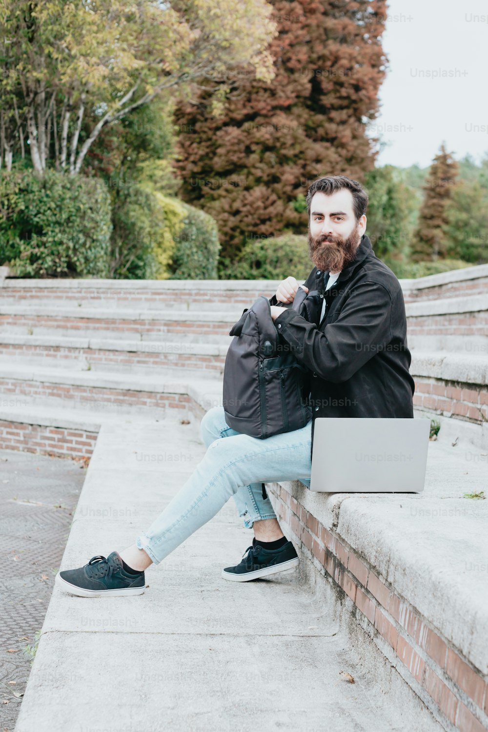 um homem com barba sentado em degraus com um laptop