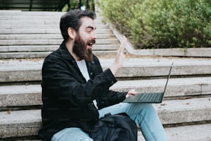 ein mann mit bart, der mit einem laptop auf stufen sitzt