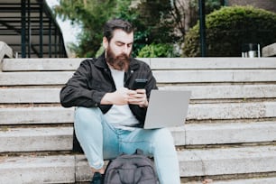 um homem com barba sentado em degraus usando um laptop