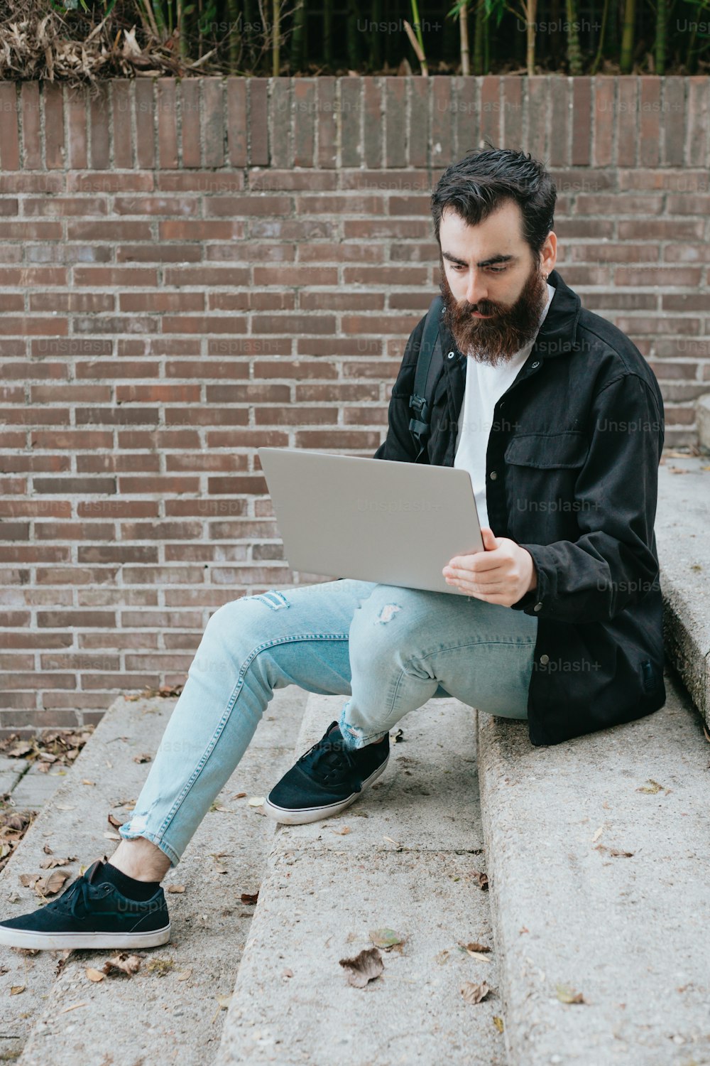 a man with a beard sitting on steps using a laptop