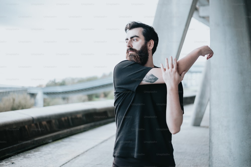 a man with a beard and tattoos standing next to a wall