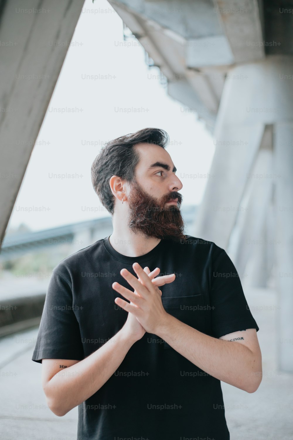a man with a beard standing in front of a bridge