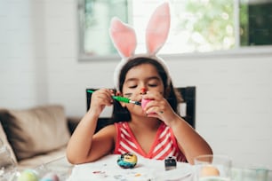 Feliz Páscoa! Uma linda menina criança pintando ovos de Páscoa. Família feliz se preparando para a Páscoa. Menina criança pequena bonito que usa orelhas de coelho no dia de Páscoa