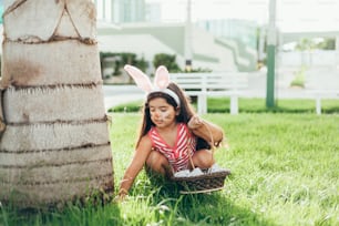 Cute little girl with bunny ears and basket of Easter eggs in the garden. Easter egg hunt