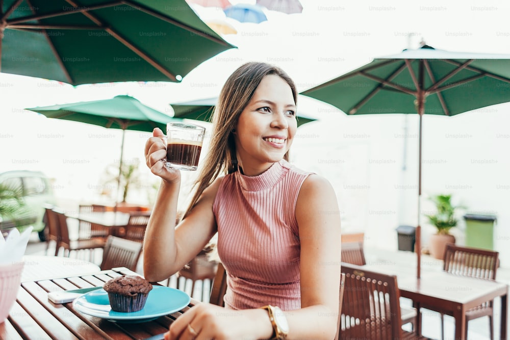 屋外のカフェに座ってコーヒーとケーキで朝食をとる若い女性