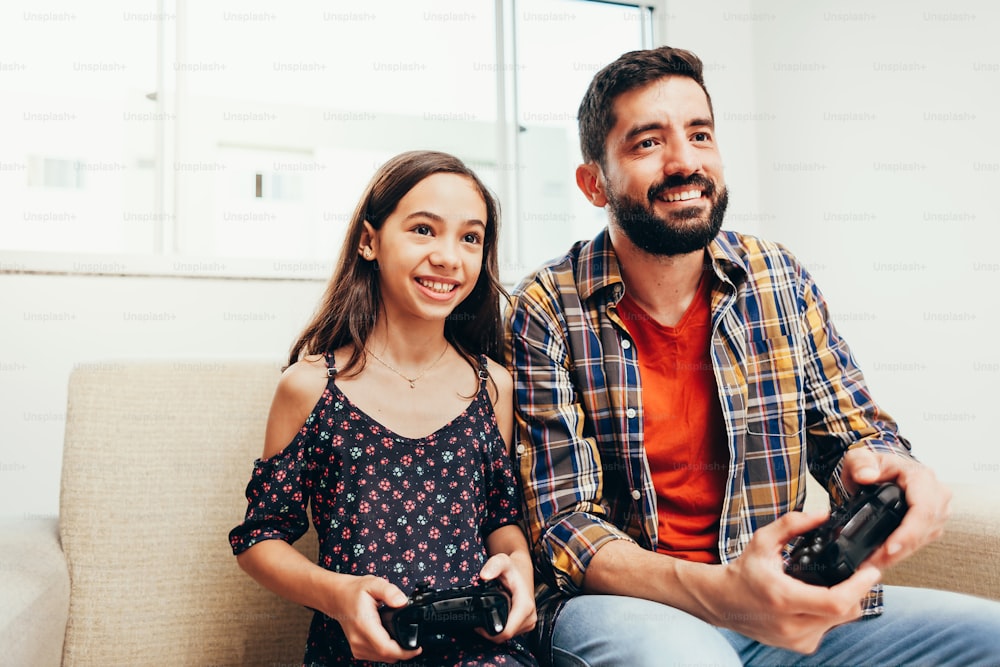 Padre e hija sonrientes jugando videojuegos en casa