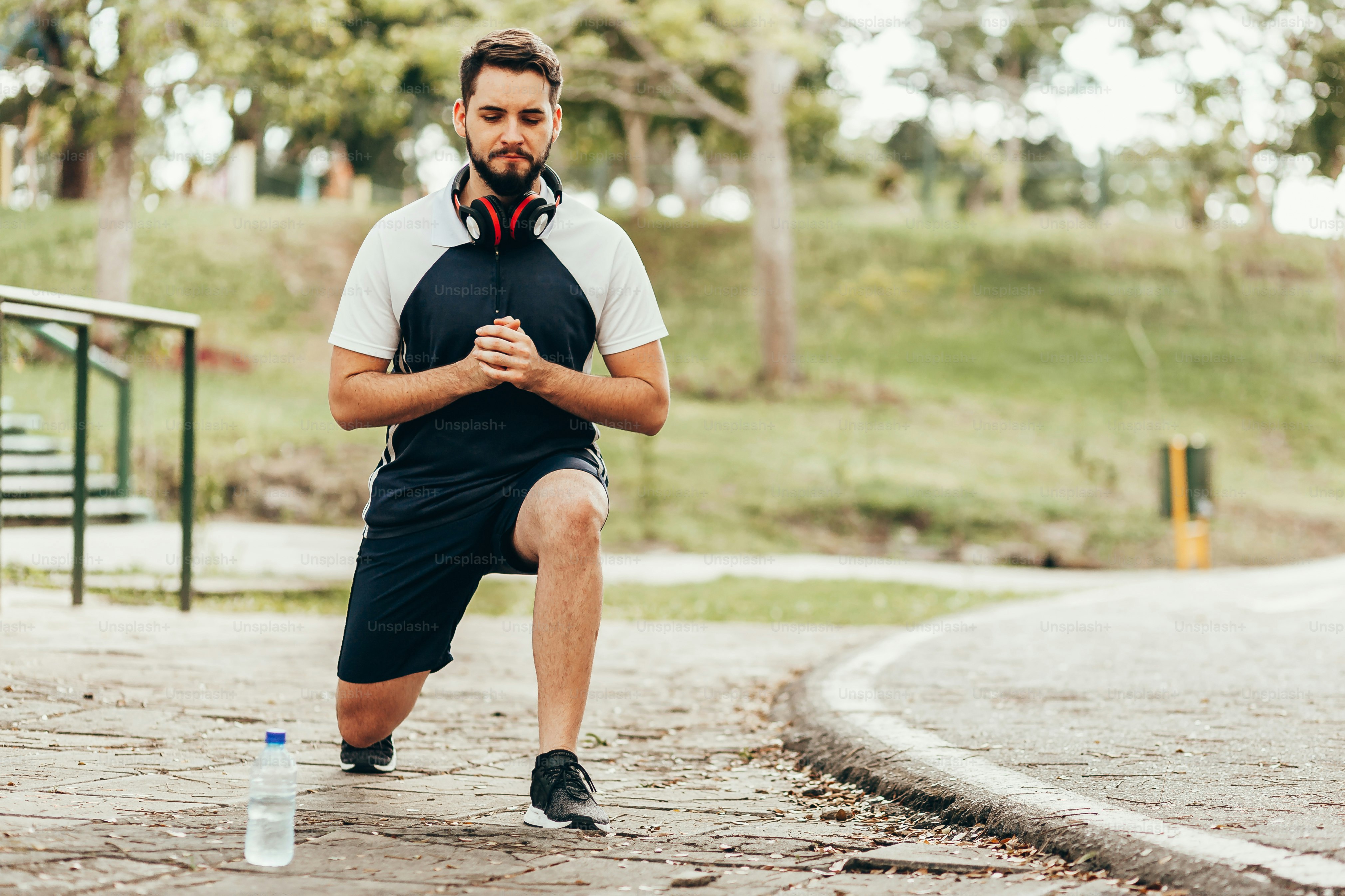 Homem vestindo roupas esportivas fazendo agachamentos em parque público.