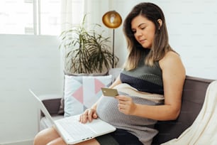 Concept d’achat en ligne. Femme enceinte avec ordinateur portable et carte de crédit achetant des articles pour bébé sur Internet