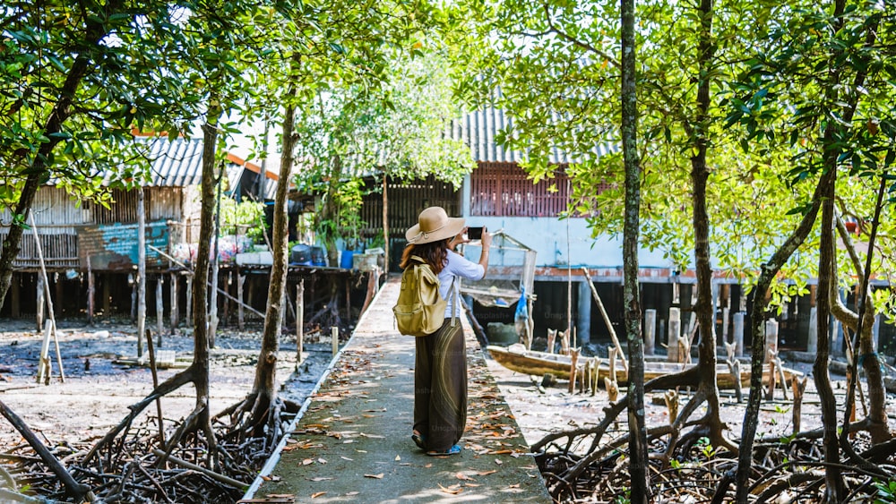 パンガー - パンガーの農村の村人の生活の道を写真を撮って歩く女の子の観光客。夏、湖、休日、旅行タイ。バックパック。携帯電話、写真。