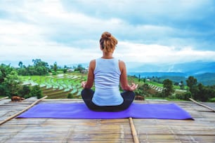 La mujer asiática se relaja en las vacaciones. Juega al yoga. En el paisaje del balcón Campo Natural