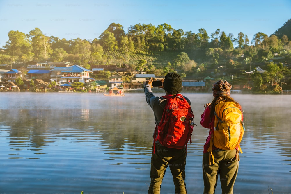 아침에 호수에 떠오르는 안개를 서서 바라보고 있는 아시아인 커플. 여행 반 락 타이 마을, 태국의 매 홍 손. 호수 사진 찍기