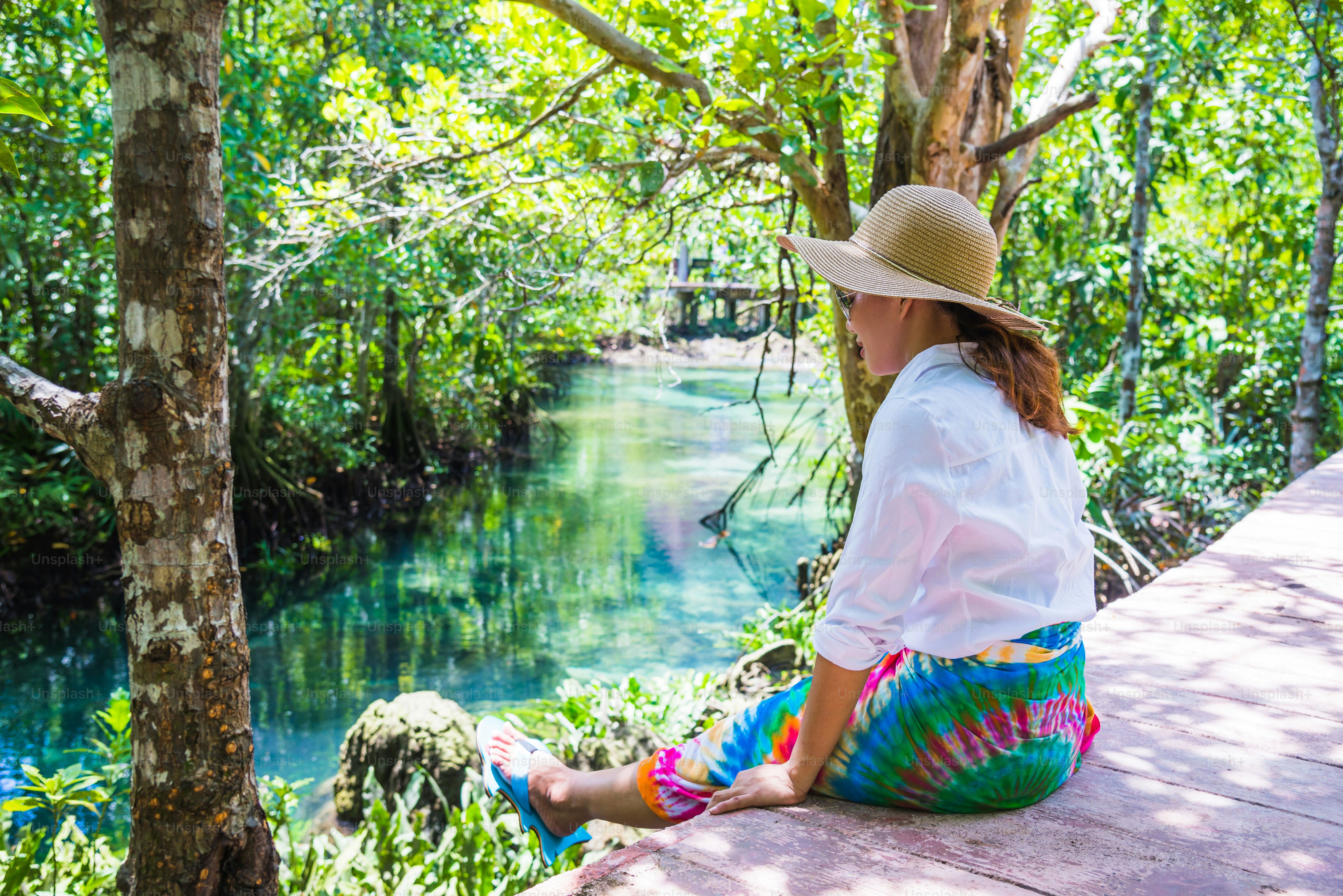 Asian women travel relax, travel nature in the holiday. Nature Study in the forest. women happy enjoying sitting and watching the lake mangrove forest. tha pom-klong-song-nam at krabi. summer