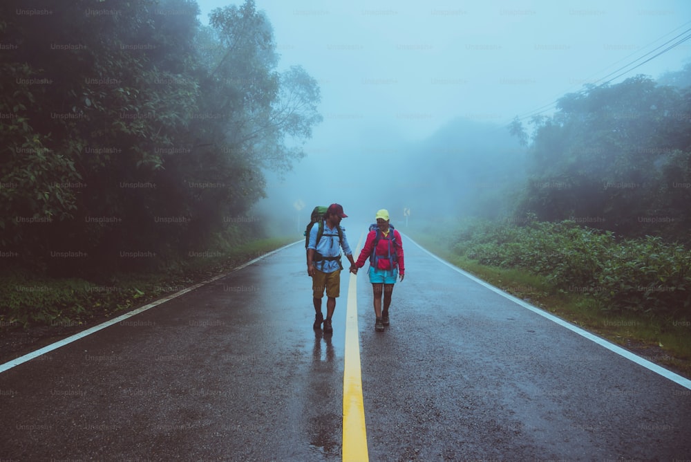 Lover asian man and asian women travel nature. Walk on the road route. traveling nature happily. Amid the mist rainy. in the rainy season.