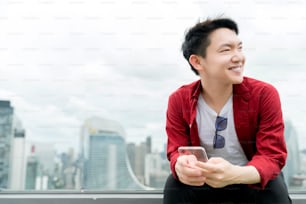 joven asiático casual relax camisa roja de mano sostén el teléfono inteligente de vidrio con fondo de la ciudad urbana centro de negocios ideas de ideas de tecnología