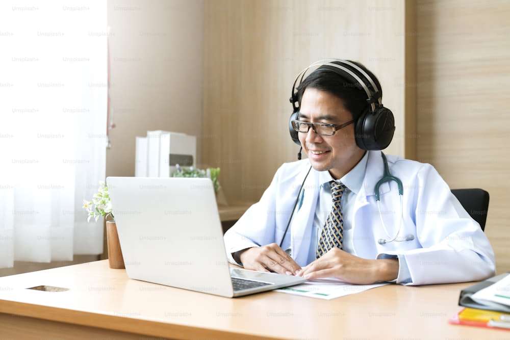 Young attractive Asian male doctor diagnosis talking and looking to camera in video conference ,Positive doctor waving and having online consultation on digital tablet laptop