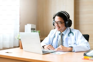 Junge attraktive asiatische männliche Arztdiagnose spricht und schaut in die Kamera in Videokonferenz, positiver Arzt winkt und hat Online-Konsultation auf digitalem Tablet-Laptop