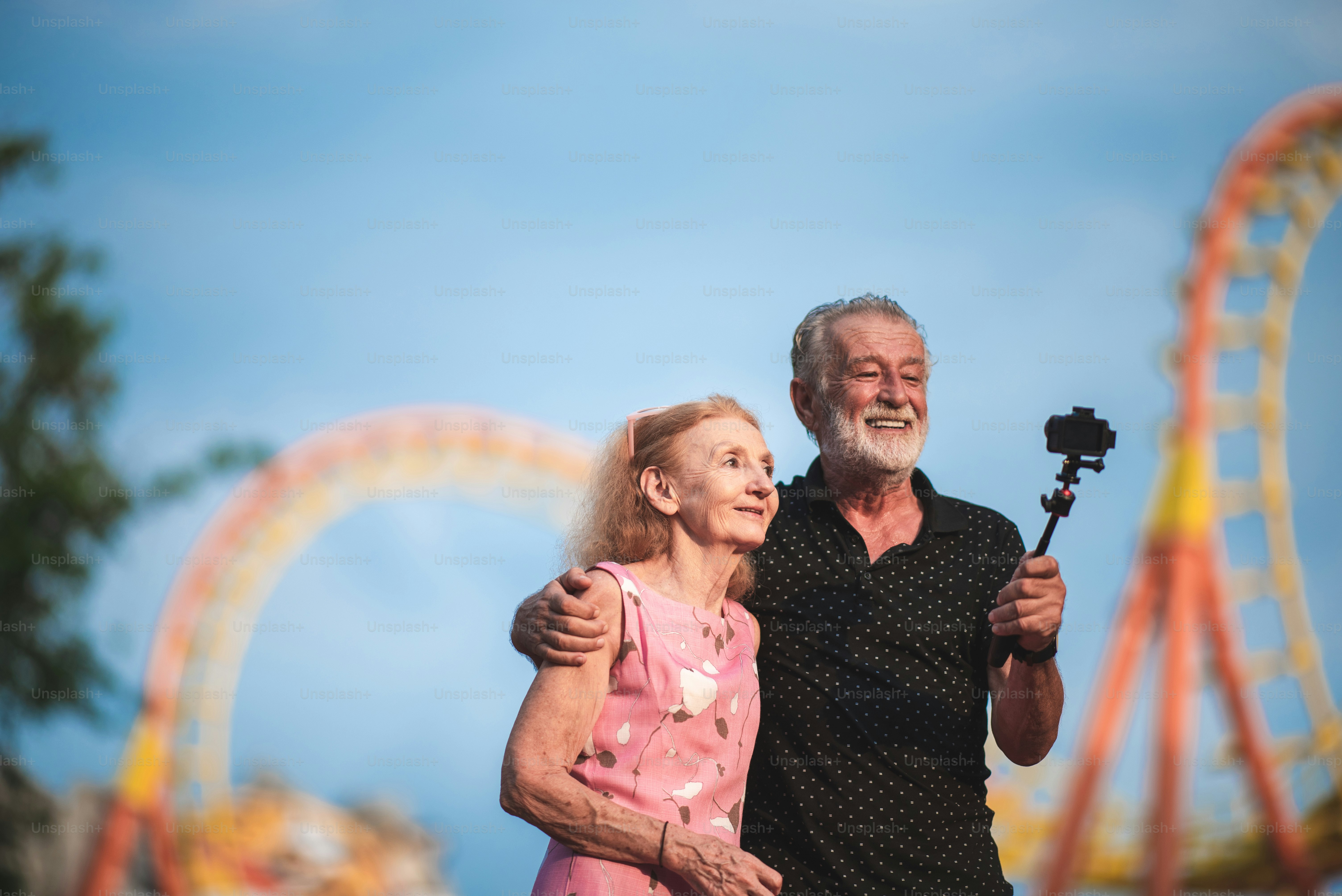 Pareja mayor tomando una selfie en el parque temático de atracciones, dos personas mayores en los años 60 que se divierten con la cámara relajándose y disfrutando al aire libre