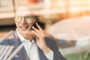 agência criativa óculos inteligentes asiáticos masculino conversa formal de pano com smartphone freelance trabalhando com laptop na área de coworking espaço de escritório com frescor com fundo de escritório desfocado