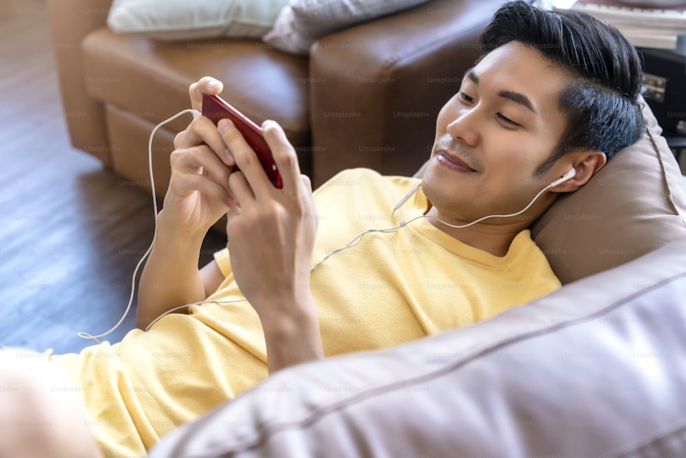 joven mano asiática jugando juegos de teléfonos inteligentes en línea casual y de ocio saliendo y jpyful tumbado en el sofá el fin de semana en casa concepto de actividades de cuarentena