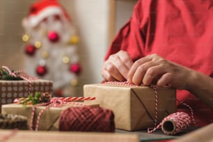 donna che fa la scatola regalo fatta a mano di Natale con la carta marrone che deforma con l'arredamento di natale sul tavolo di legno