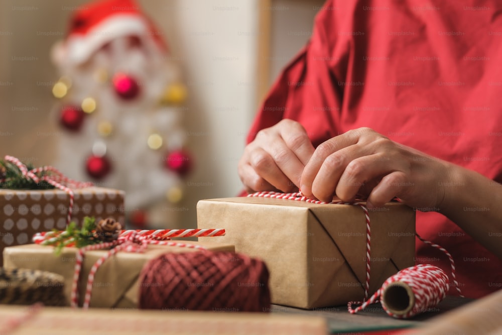 mulher que faz a caixa de presente artesanal do Natal com deformação de papel marrom com decoração de xmas na mesa de madeira