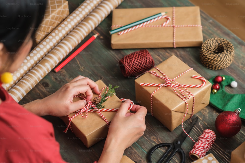 나무 테이블에 크리스마스 장식으로 뒤틀린 갈색 종이로 크리스마스 수제 선물 상자를 만드는 여자
