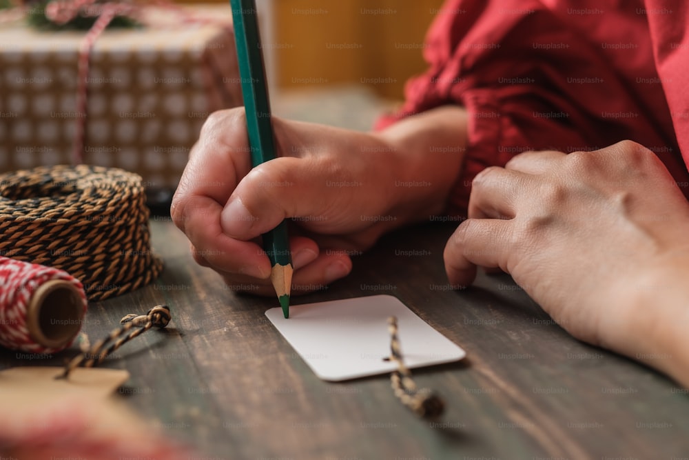 Frau schreibt Geschenkanhänger und befestigt an Weihnachtsgeschenk auf Holztisch