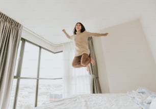 Foto de uma jovem asiática atraente feliz excitada pulando em sua cama