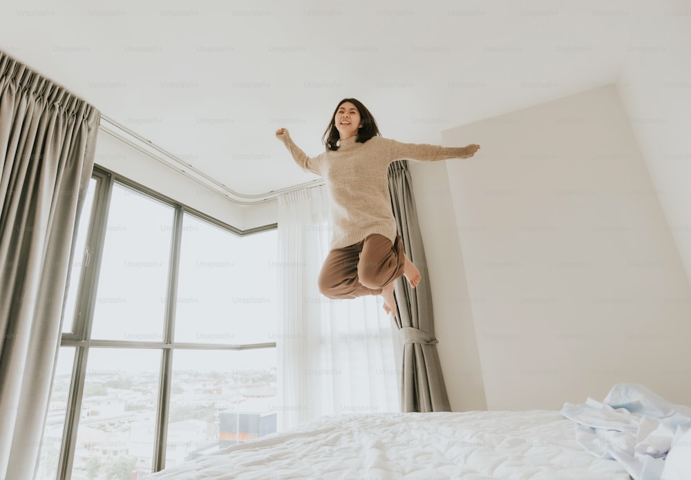 Aufnahme einer glücklichen, attraktiven jungen Asiatin, die aufgeregt auf ihr Bett springt