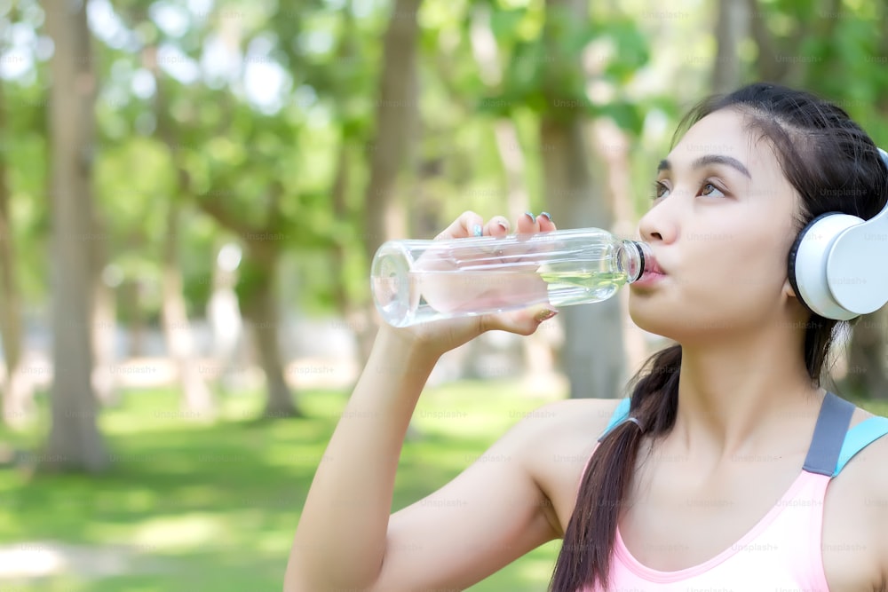 Mulher jovem asiática bebendo água após o exercício do treino.
