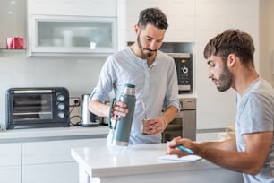 Young man writing in a paper while his boyfriend is preparing mate infusion