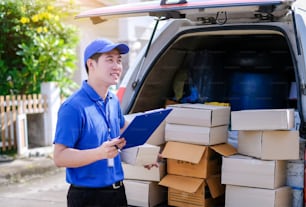 Jeune livreur en uniforme bleu vérifiant les boîtes de produits à envoyer aux clients dans des véhicules de transport.