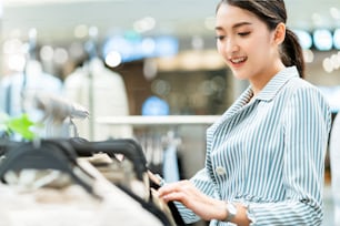 Smart attraktive asiatische Frau genießen wählen Ffitting Tuch mit Stoffträger in Boutique-Shop Einkaufszentrum Hintergrund