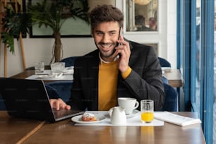 A businessman talking on his phone while he is having breakfast at a bar.