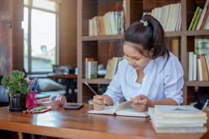 Estudiante asiática sentada y escribiendo una nota en la biblioteca de la mesa en la escuela.