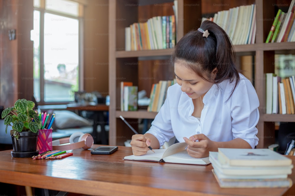 Asian female student sitting and write a note on table library at school.