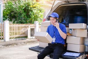 Joven repartidor con uniforme azul llama por teléfono a los clientes para entregar las mercancías.