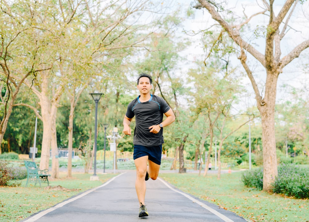 Happy healthy Asian man runner running outdoor in the park in morning