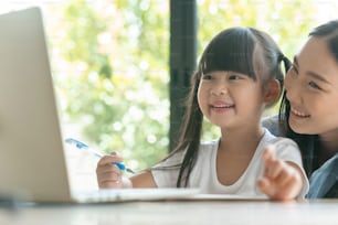 young asian mother on blue shirt enjoy teaching her adorable daughter a homework on a laptop. Asian little girl kind enjoy learning with her beautiful mother.