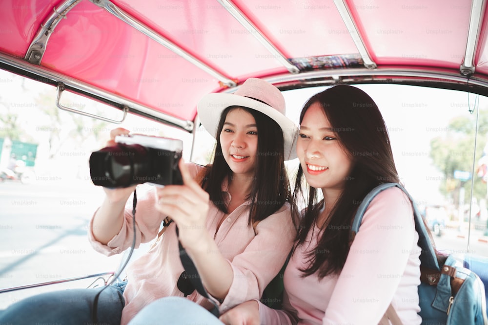 Two Asian women traveler checking photo in camera while travel by tuk tuk taxi