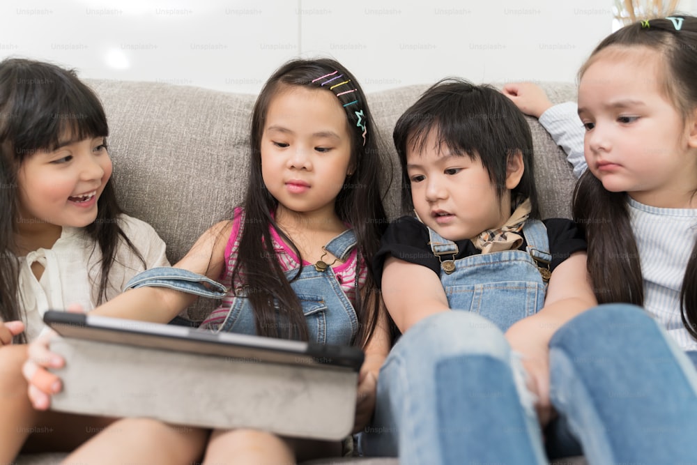 group of little children watching film movie cartoon together on digital tablet. Kids playing with tablet with friends at home.