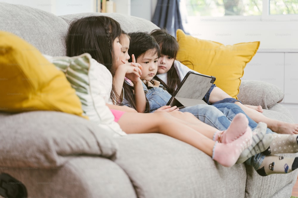 group of little children watching film movie cartoon together on digital tablet. Kids playing with tablet with friends at home.