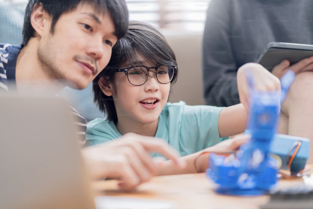 study at home concept,asian boy child with father and mother successful control robot arm on Digital tablet and computer keyboard, happy family getting a lesson in coding control robotics at home