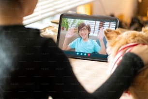 videollamada al concepto de distanciamiento social familiar, gesto de la mano de la mujer asiática y saludo a su hijo con conversación de amor y felicidad hablando en línea desde la tableta con un pequeño amigo perro