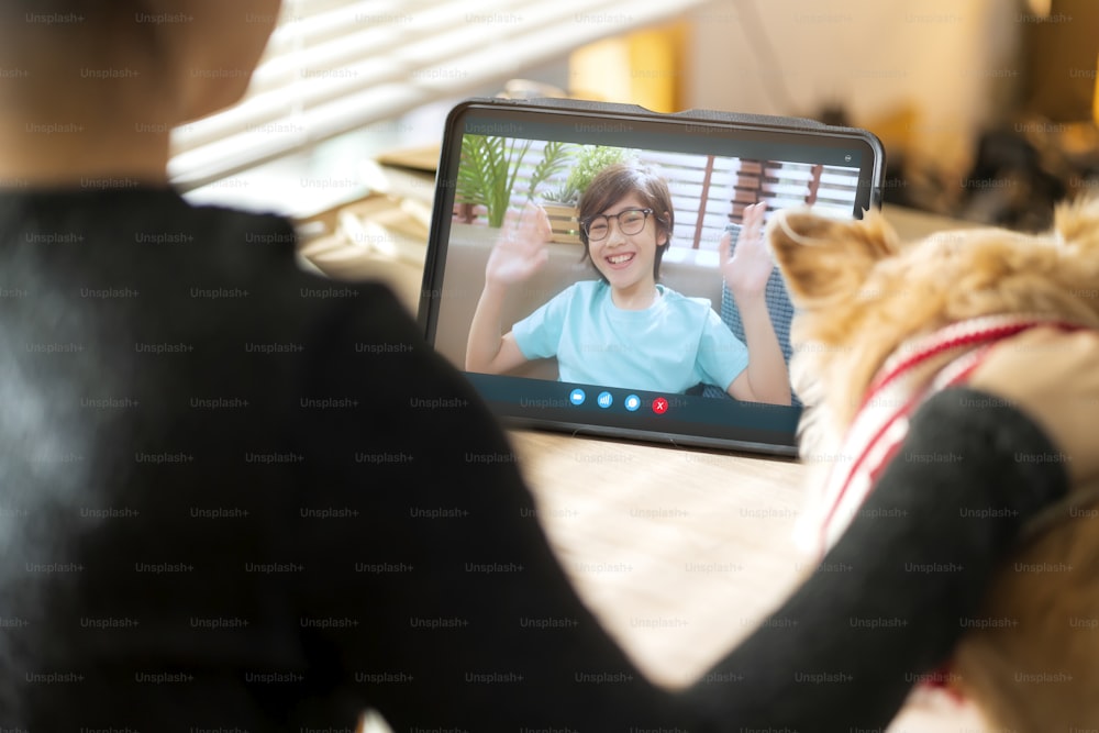 videollamada al concepto de distanciamiento social familiar, gesto de la mano de la mujer asiática y saludo a su hijo con conversación de amor y felicidad hablando en línea desde la tableta con un pequeño amigo perro