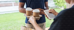 Asian Woman using pen signing digital signature on mobile tablet after receive hot drink or coffee from African American delivery man in blue uniform from courier at door of home. Panoramic Web banner
