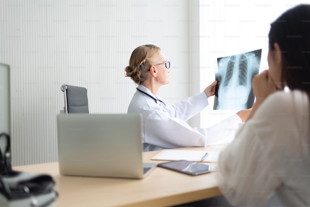 Medico donna senior che esamina e guarda la pellicola a raggi X del suo paziente in una stanza medica.