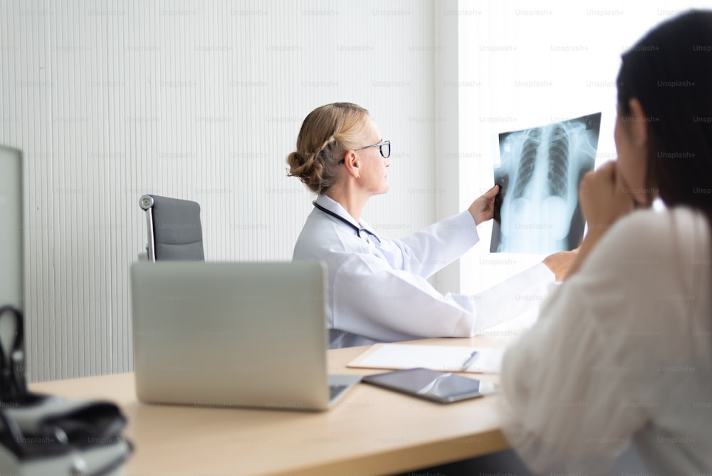 Senior Female doctor examining and looking to X-ray film of her patient at a medical room.